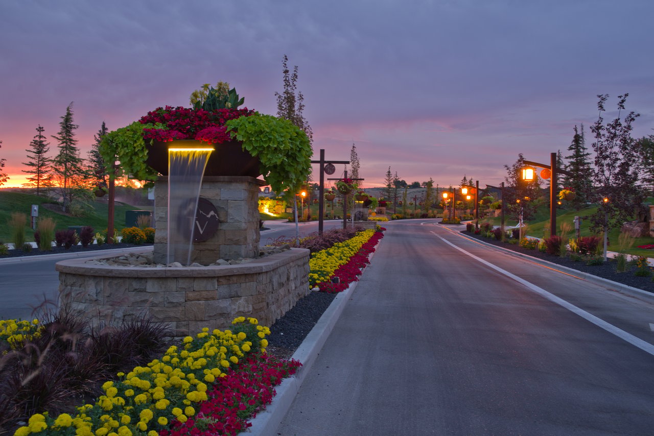 Terra View development entrance with a stone fountain and colorful flowerbeds beside the road at dusk.