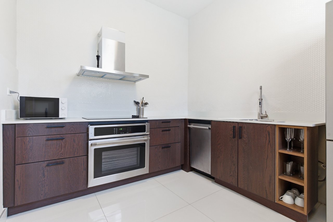 Modern kitchen with dark wood cabinets, white counters, and a built-in oven beneath a stainless range hood.