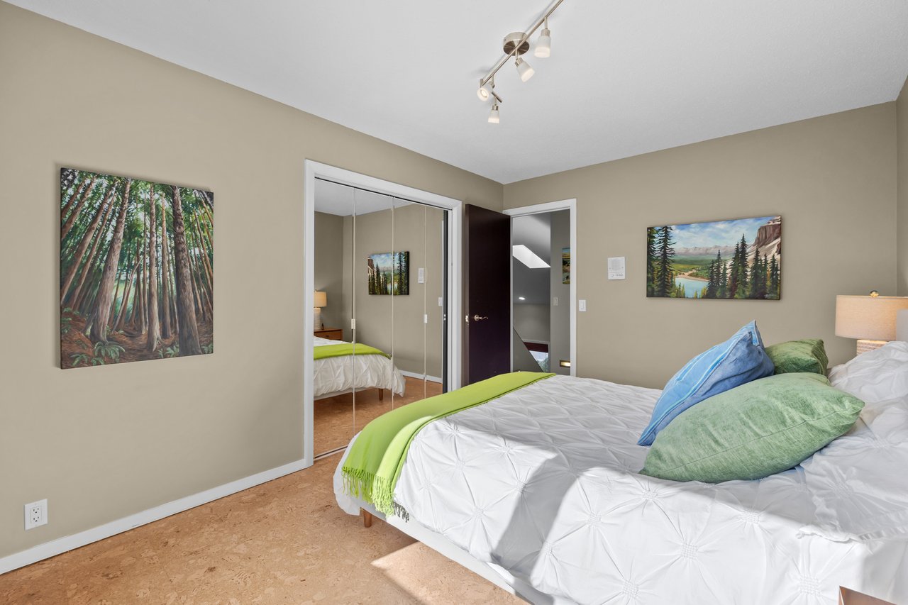 Bedroom with mirrored closet doors, cork flooring, and a white bed with colorful pillows.