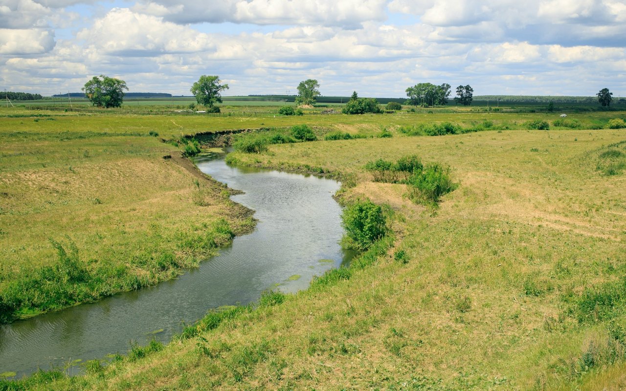 A winding stream crosses open grassy fields beneath a cloudy sky.