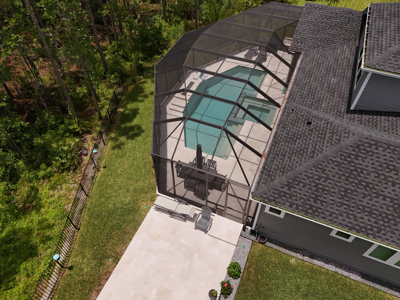 Aerial view of a screened backyard pool beside a paved patio and tree-lined lawn.