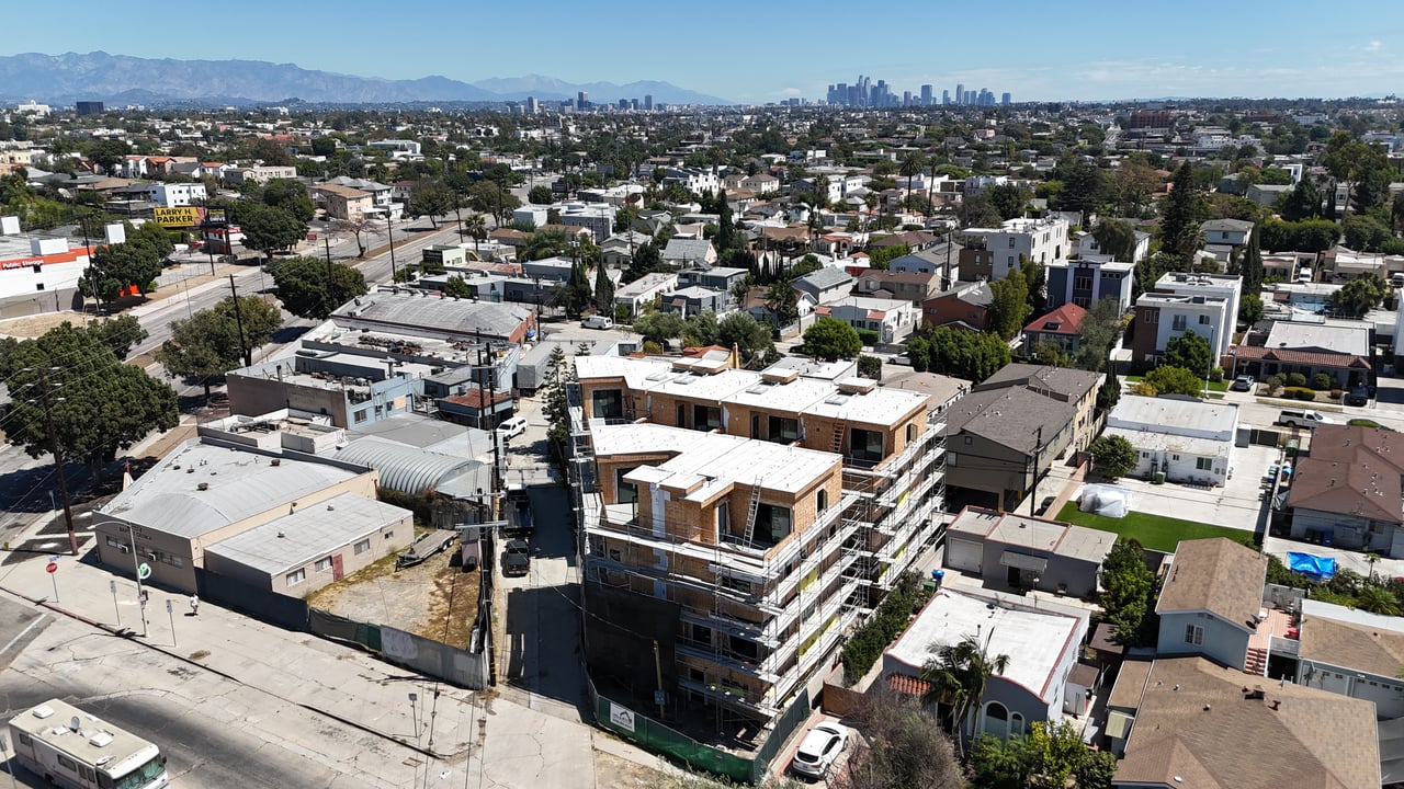Aerial view of a multi-story building under construction, with scaffolding and the Los Angeles skyline in the distance.