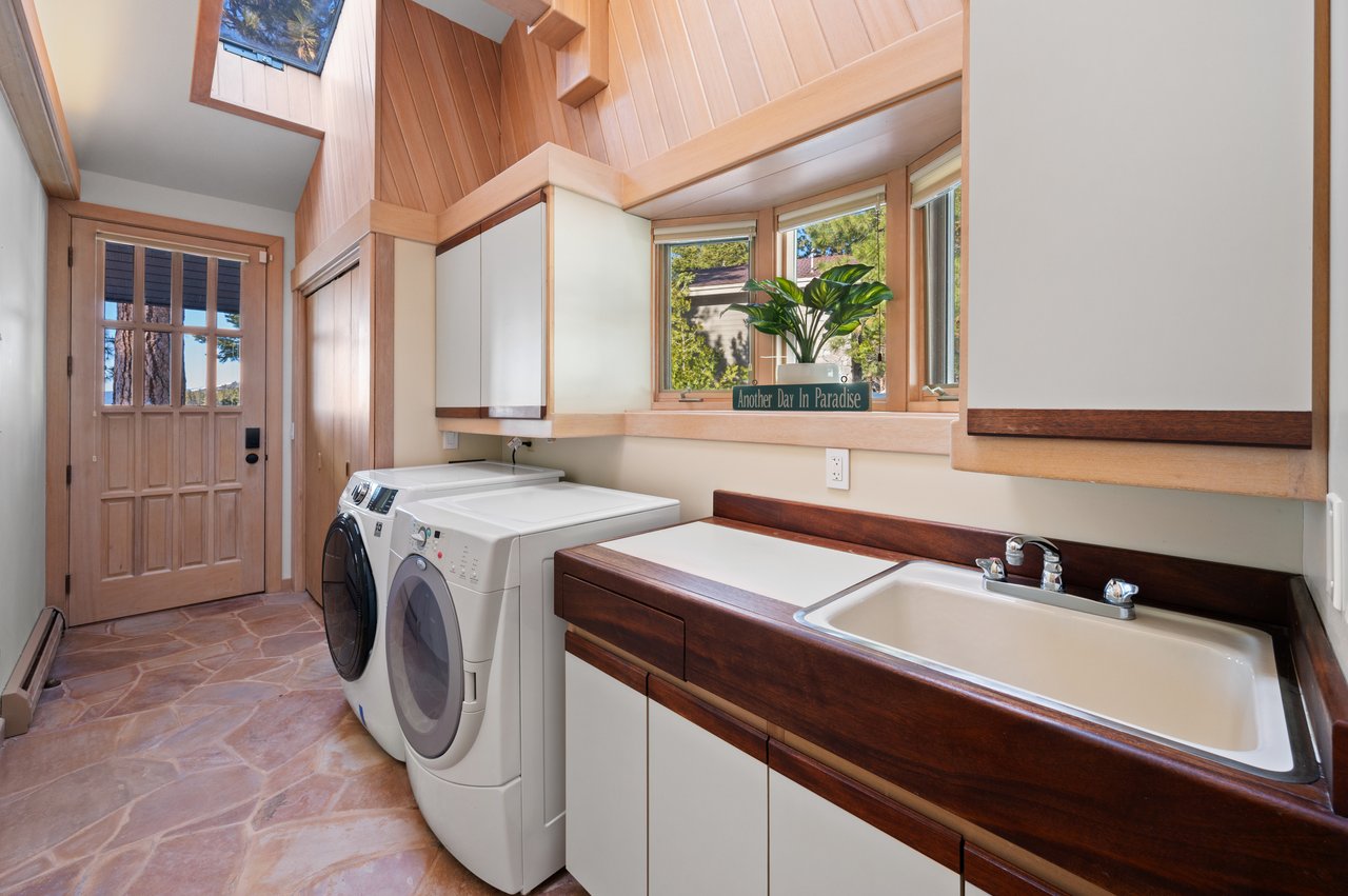 Laundry room with front-loading washer and dryer, deep utility sink, and warm wood paneling.