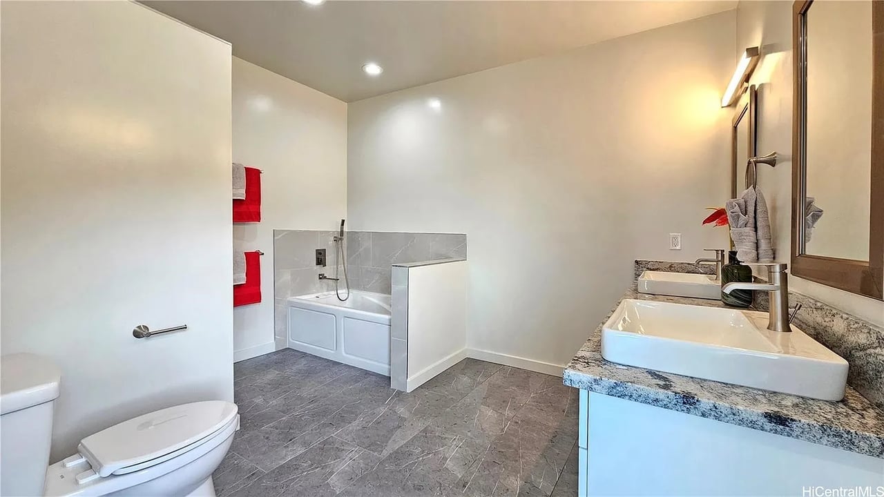 Bathroom with a tiled bathtub enclosure, gray floors, and a granite double-sink vanity.
