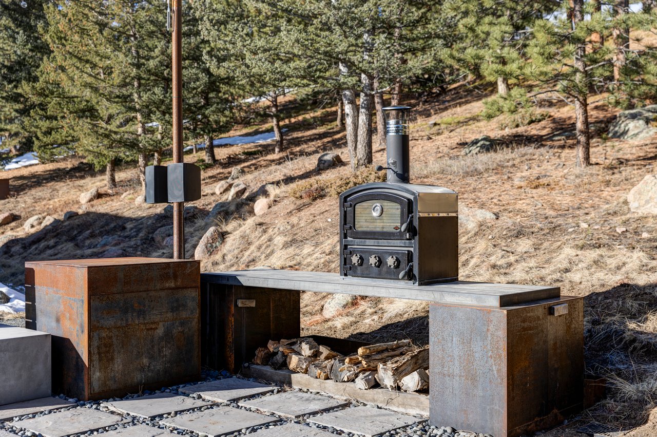 Built-in outdoor pizza oven and grill station with weathered steel finishes and firewood storage