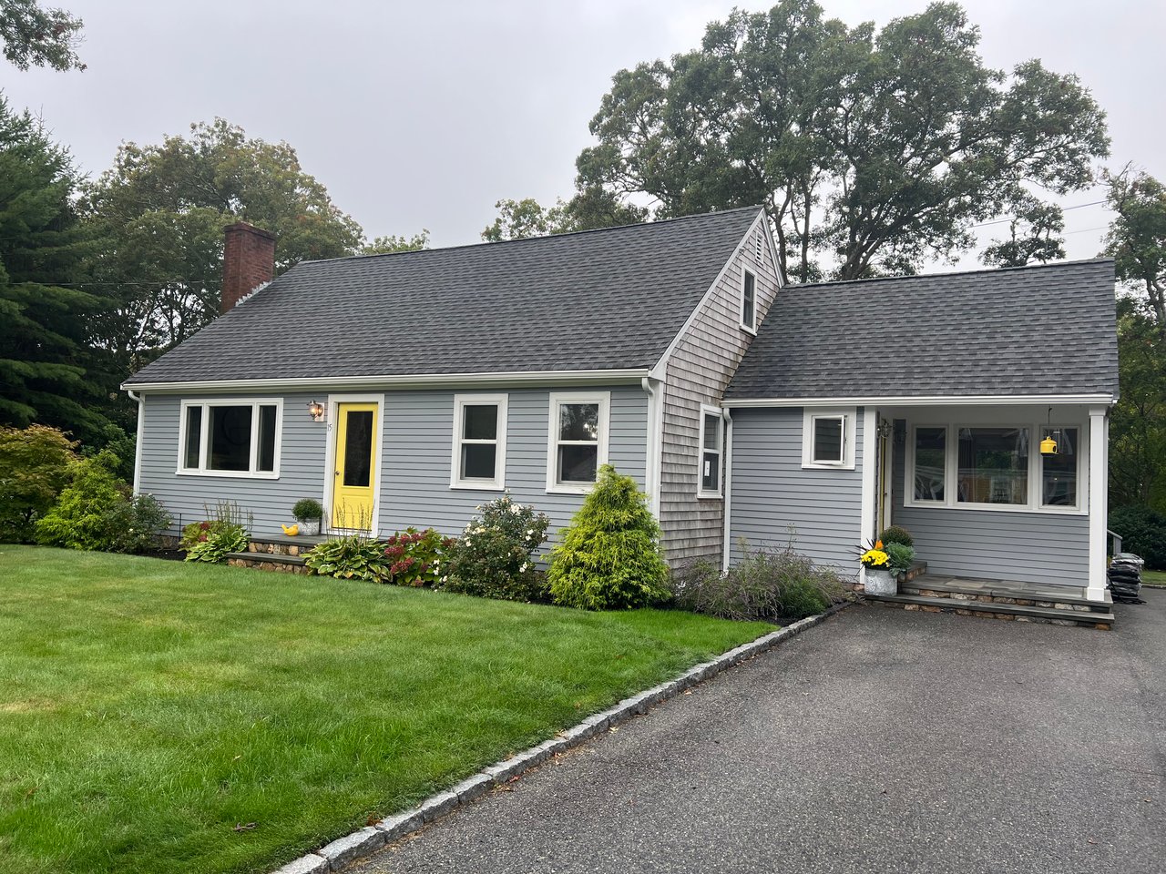 Gray Cape Cod-style home with a yellow front door, landscaped garden, and attached covered porch.