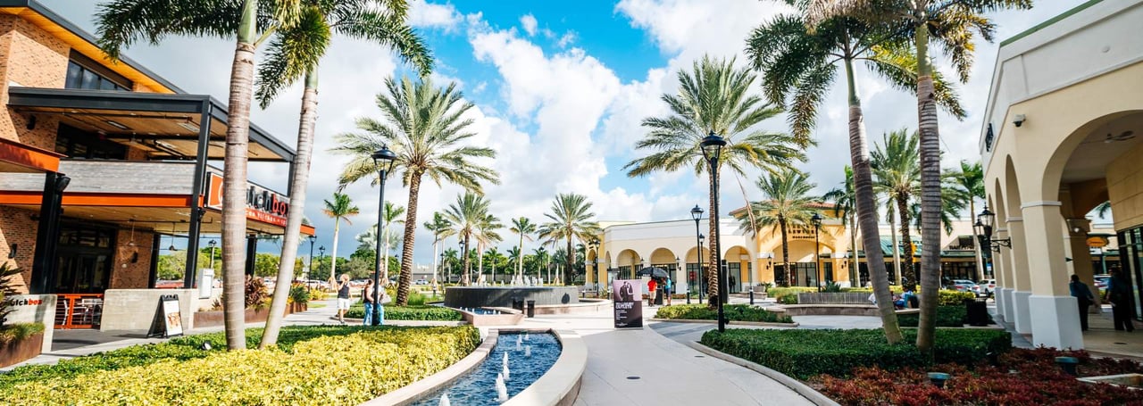 Outdoor view of Sawgrass Mills shopping center in Sunrise, Florida with palm trees, fountains, and shops.