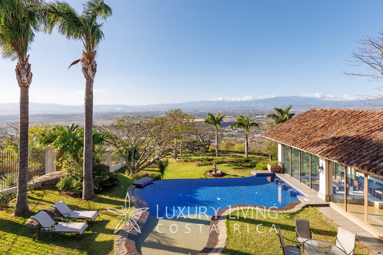 Outdoor pool and garden beside a tiled-roof terrace, with palm trees and a wide valley view.