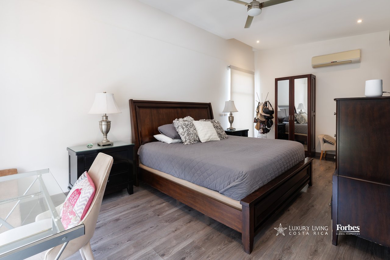 Furnished bedroom with a large dark wood bed, gray quilt, ceiling fan, and mirrored wardrobe.