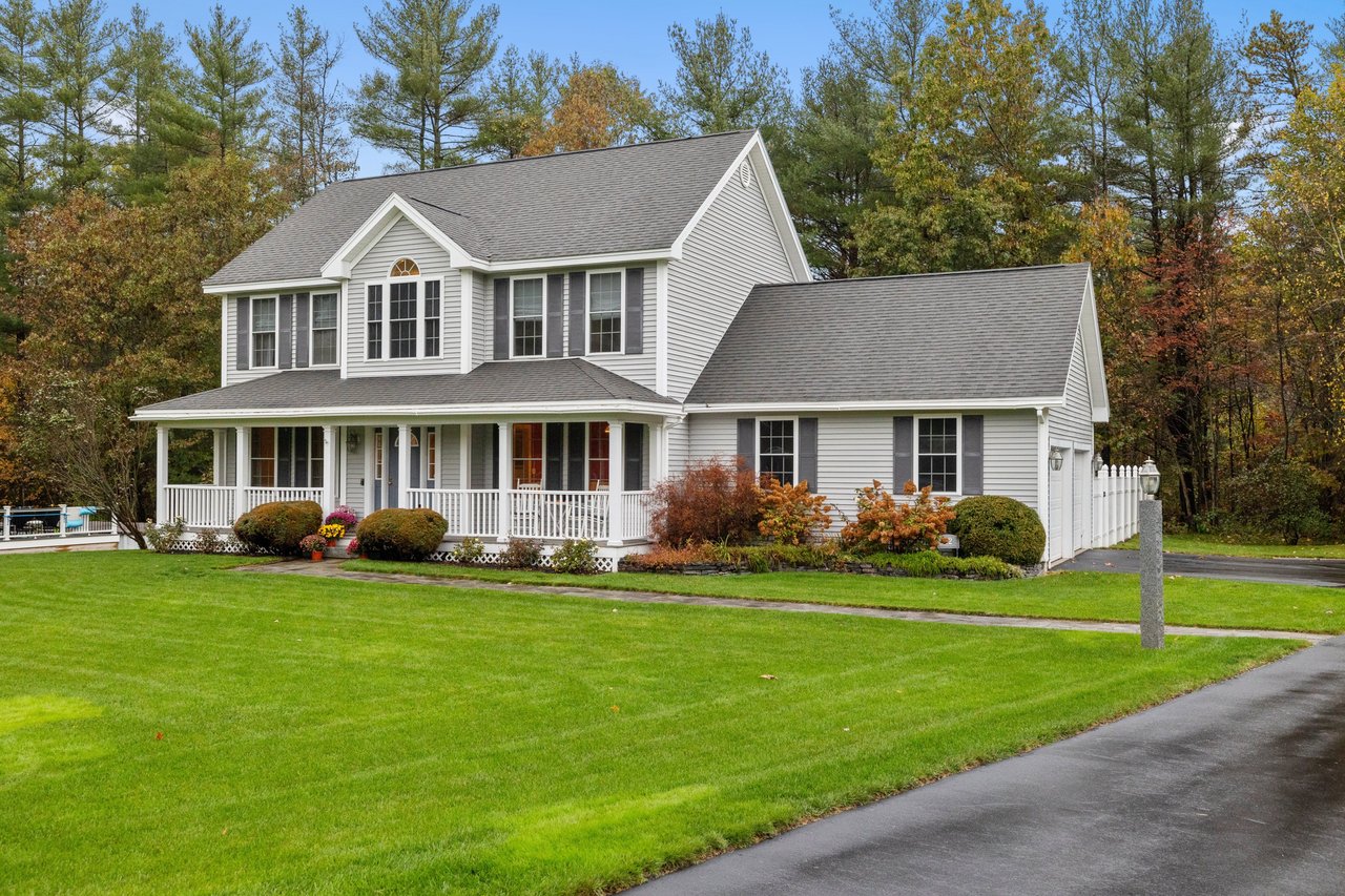 White two-story house with a covered porch, dark shutters, and a broad lawn.