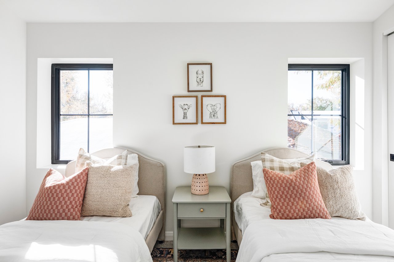 Childen's bedroom with two twin beds, large windows above, and a sage end table with a small pink lamp.