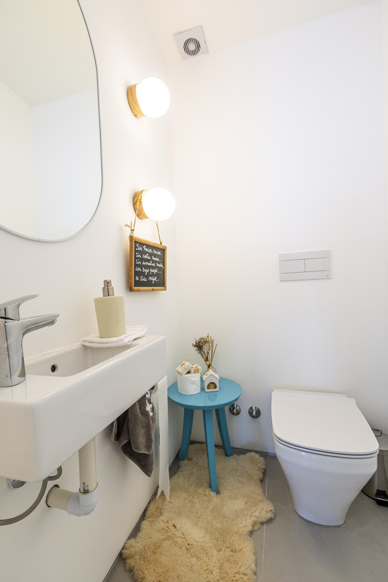 Compact bathroom with a white sink and toilet, rounded mirror, and blue side table.