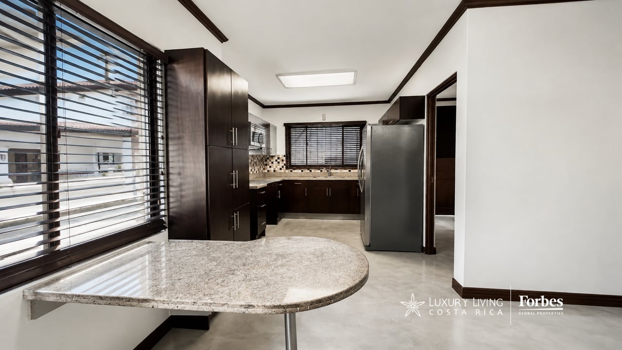 Kitchen with dark wood cabinetry, stainless steel refrigerator, and a curved granite breakfast counter.