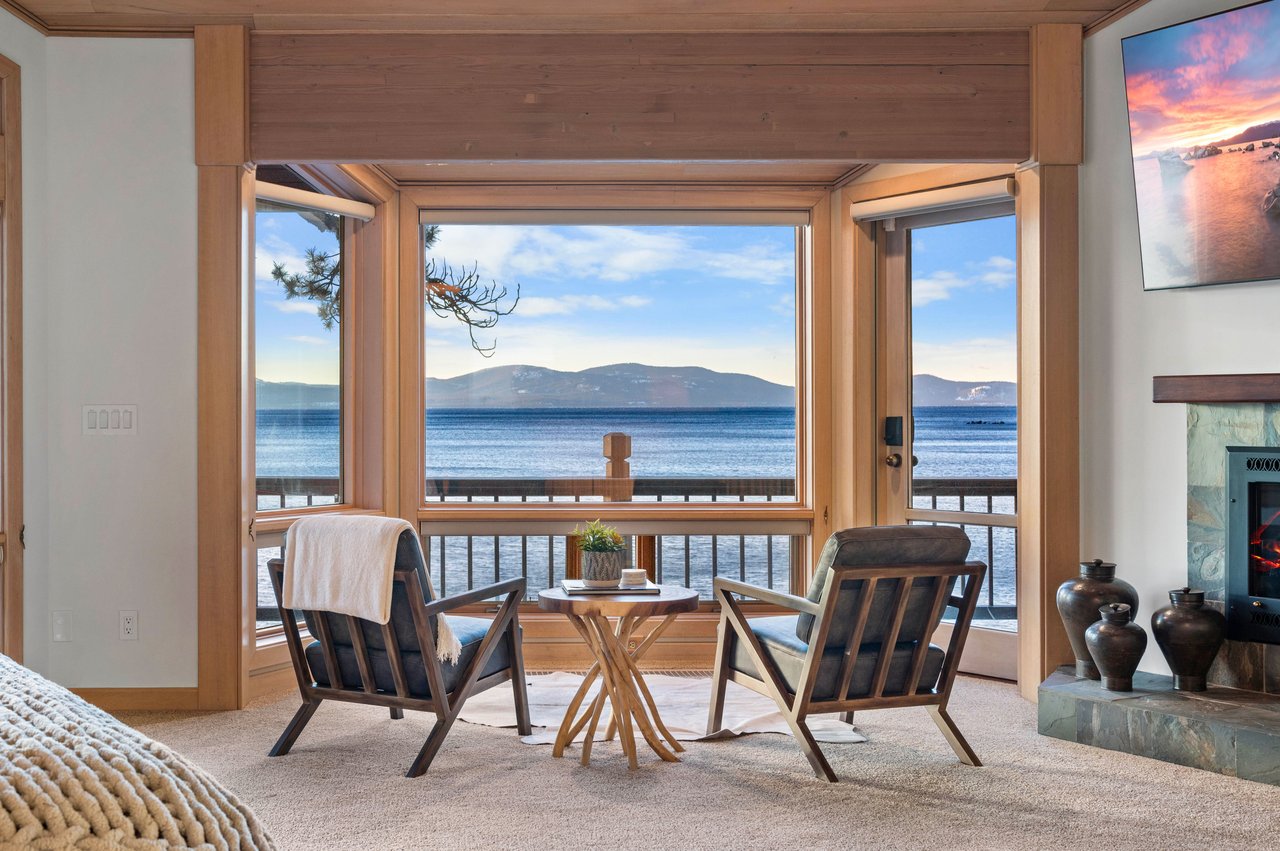 Lakeside sitting area with two chairs facing broad windows overlooking the water and distant mountains.