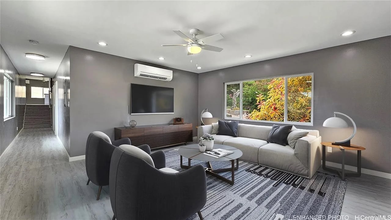 Living room with a light sectional, dark armchairs, patterned rug, and wide window overlooking greenery.