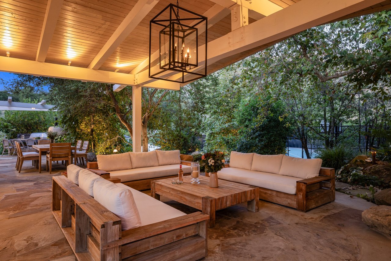 Covered patio with wood-framed sofas, a timber ceiling, and leafy garden views.