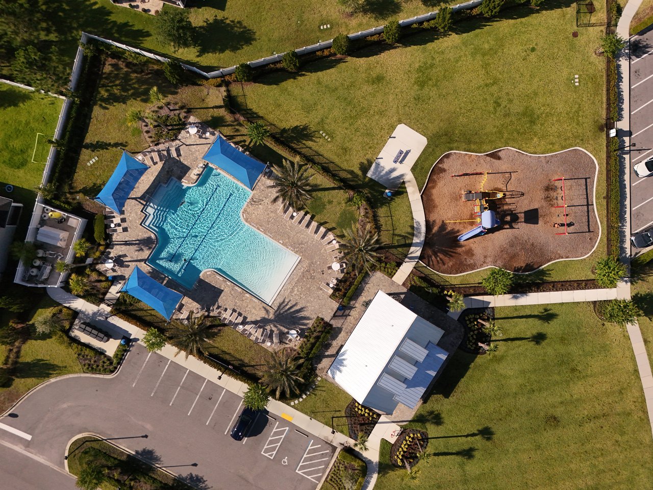 Community pool and playground with blue shade canopies, walking paths, and nearby parking.