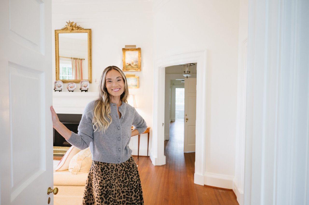 Ann Hay Hardy smiling in a living room doorway, wearing a gray cardigan and leopard-print skirt.