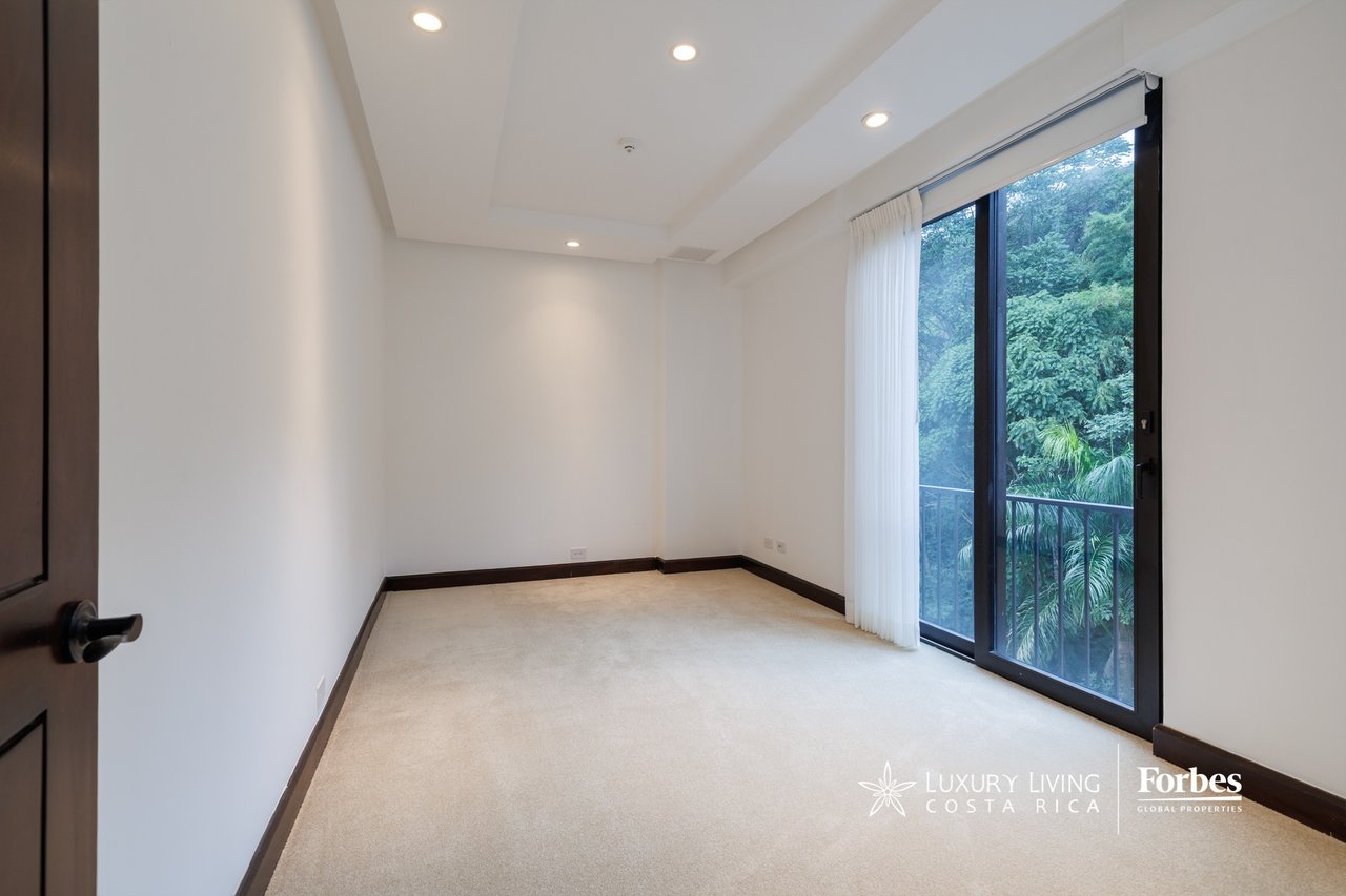 Empty carpeted room with recessed lights and sliding glass doors overlooking greenery.