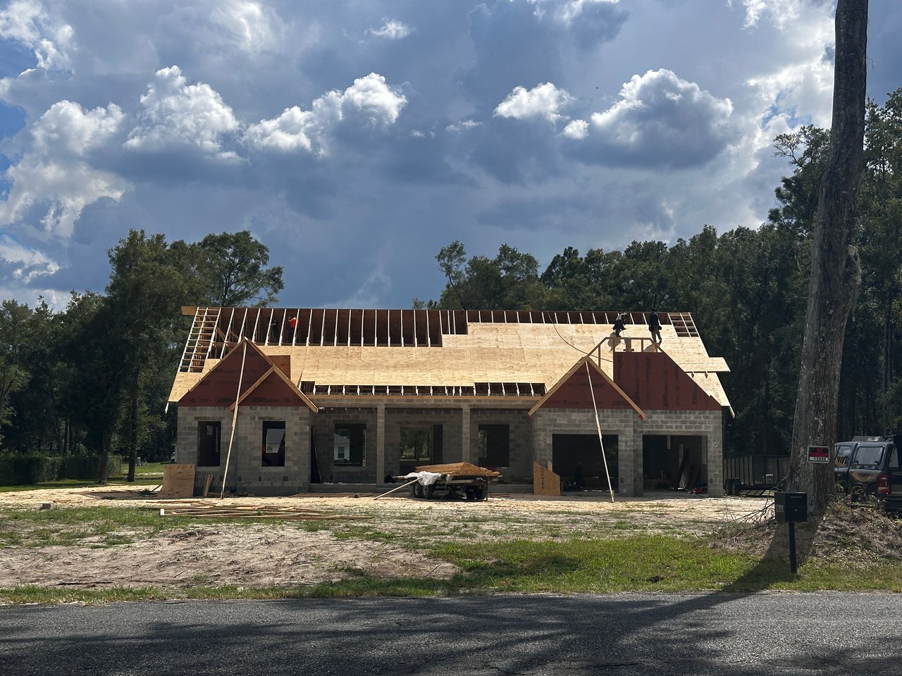 House under construction with exposed roof framing and workers on the roof