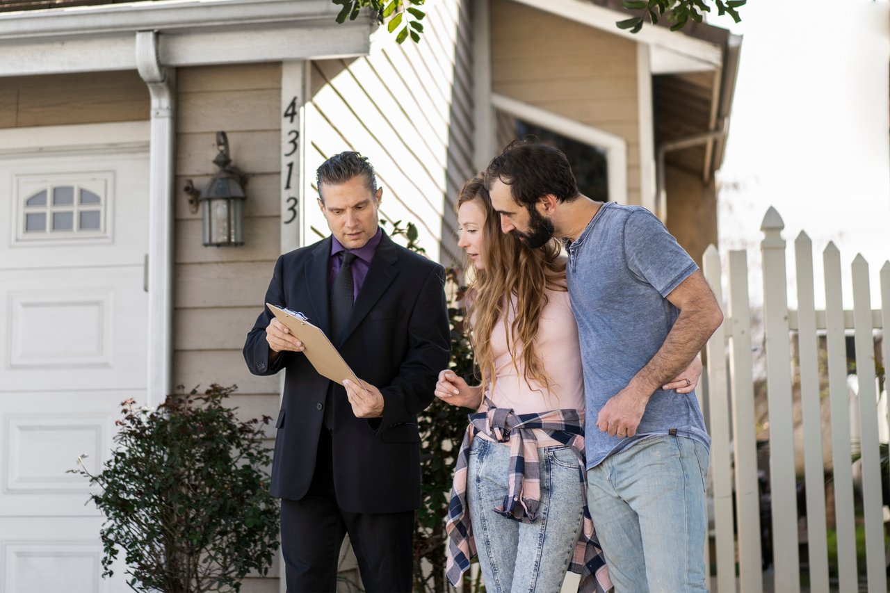 Home buyers reviewing documents with a real estate agent outside a house in North Texas