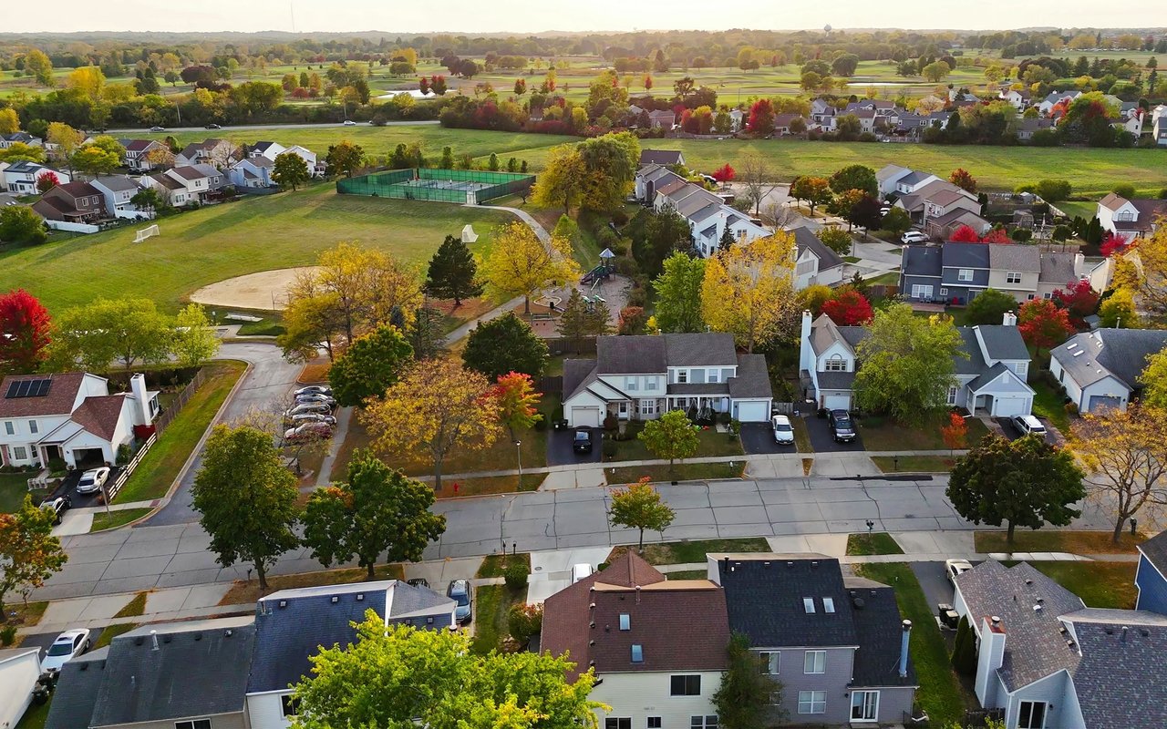 Aerial view of suburban homes and a park among colorful autumn trees.