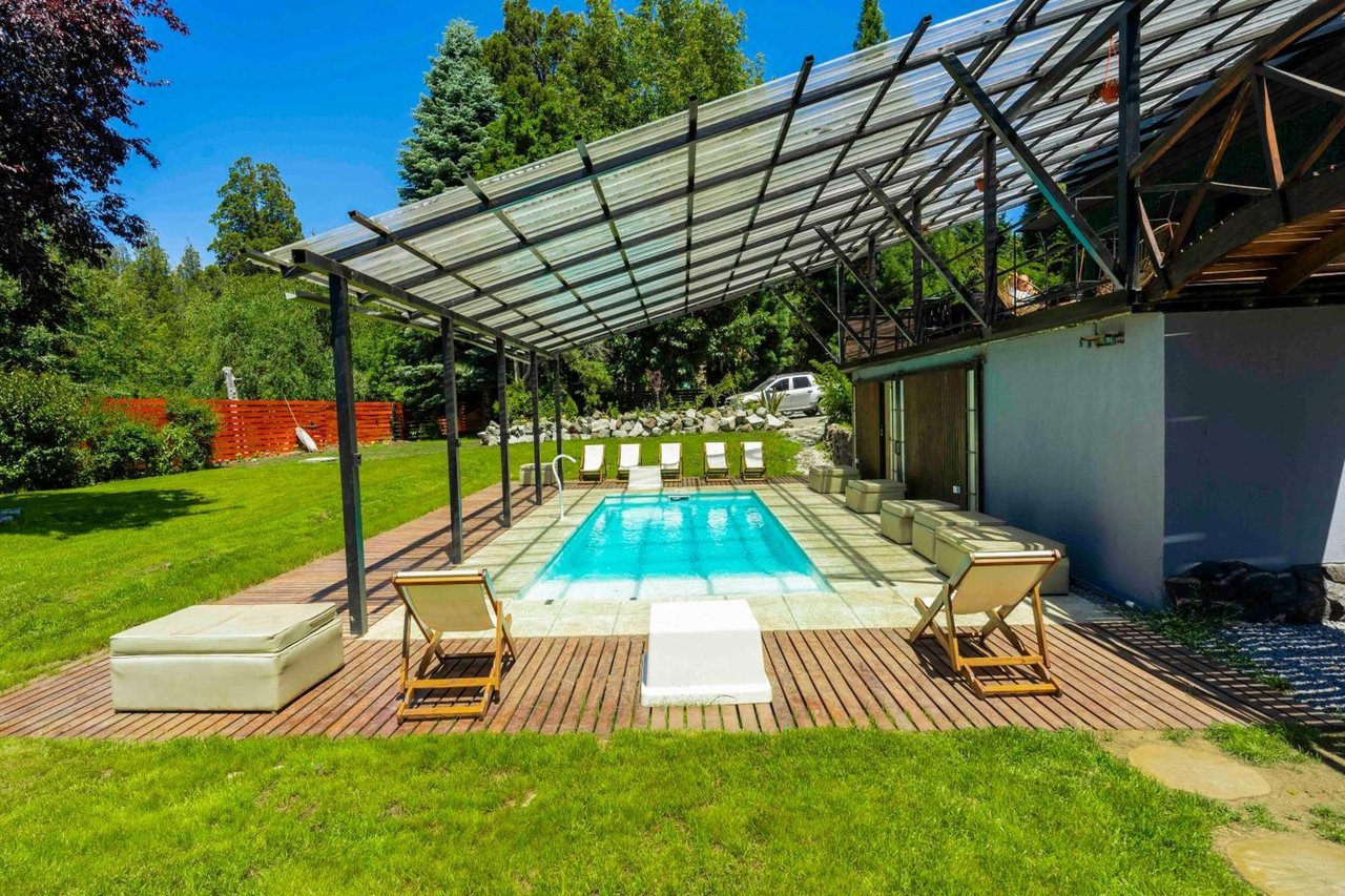 Outdoor pool beneath a translucent canopy, with wooden decking, loungers, and a green lawn.