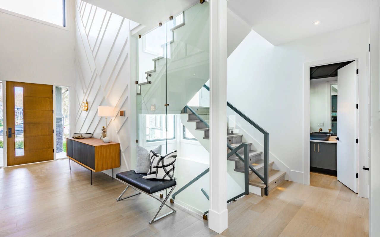 Modern foyer with a glass-enclosed staircase, wood front door, and black bench.