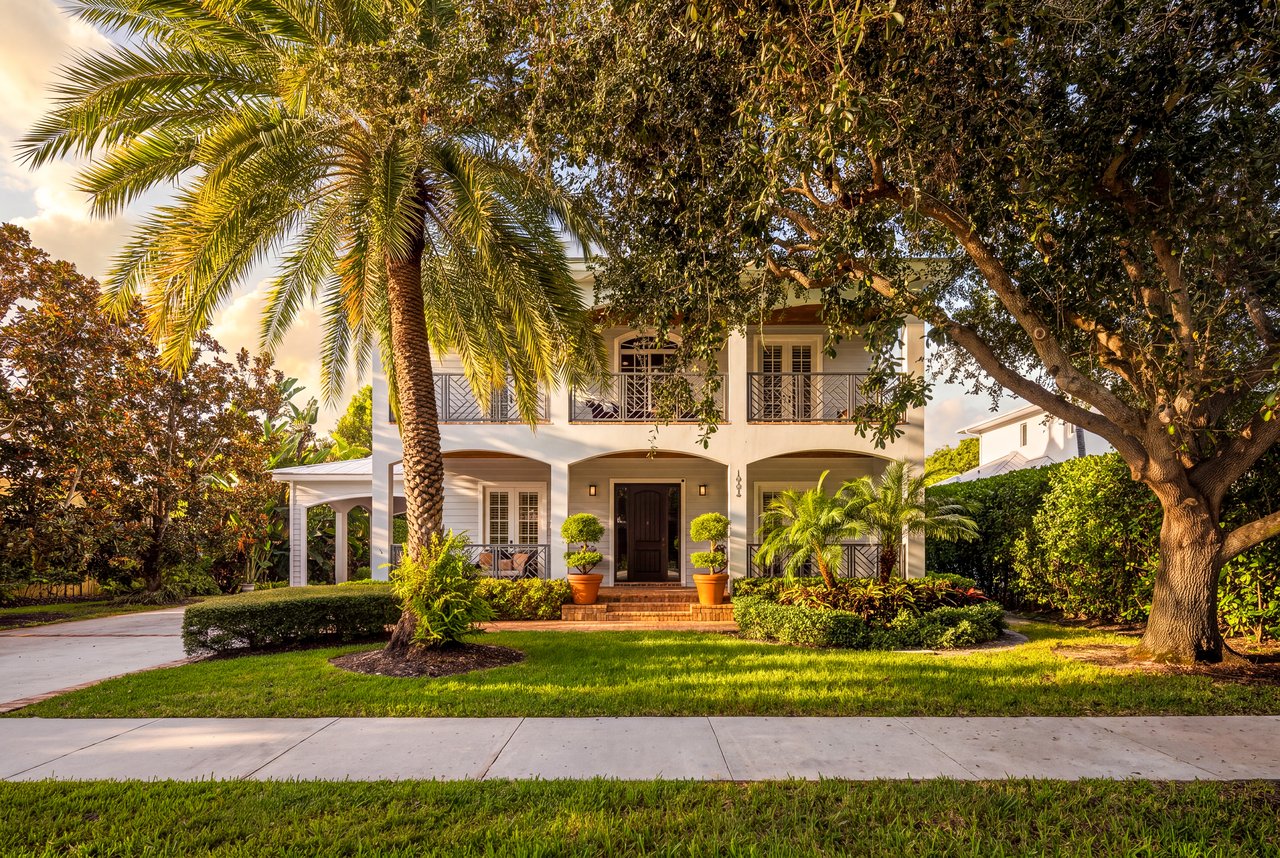 Two-story white home with upper balconies, framed by palm and oak trees.
