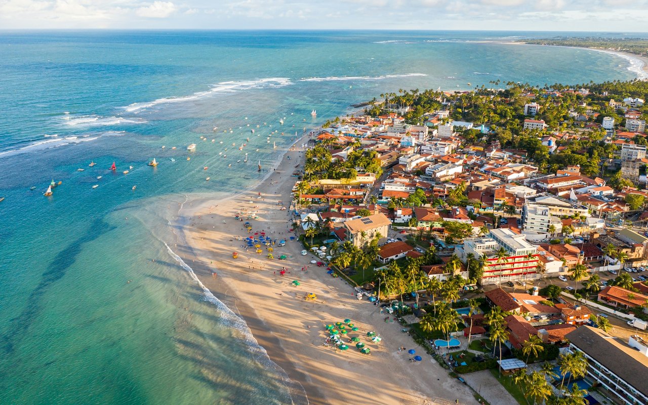 Aerial view of a palm-lined coastal town and sandy beach beside turquoise water.
