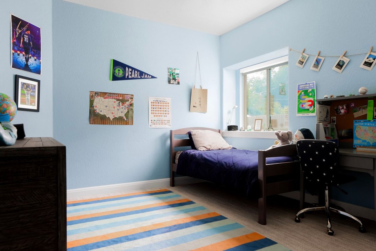 Blue bedroom with a single bed, desk, star-patterned chair, and colorful striped rug.