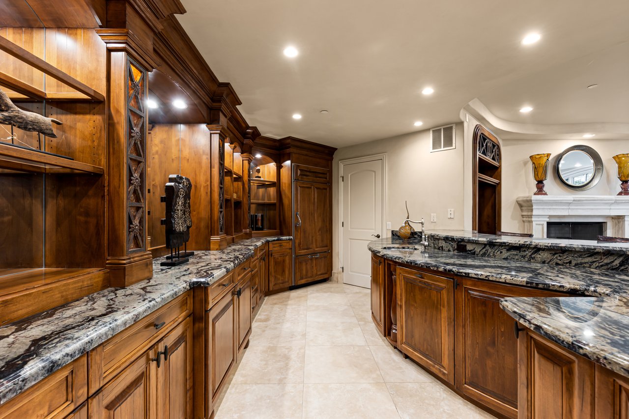 Luxury kitchen with dark wood cabinetry, patterned stone counters, and a large curved island.