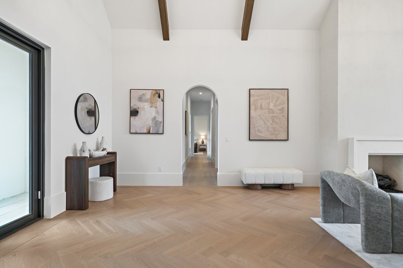 Bright living room with exposed wood beams, herringbone floors, an arched hallway, and a fireplace.