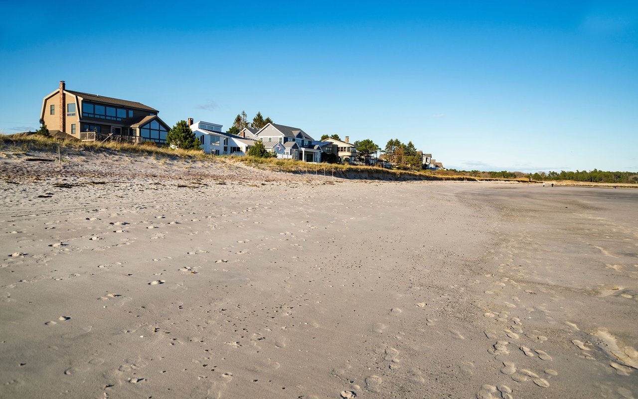 Sandy beach with coastal homes along the dune beneath a clear blue sky.