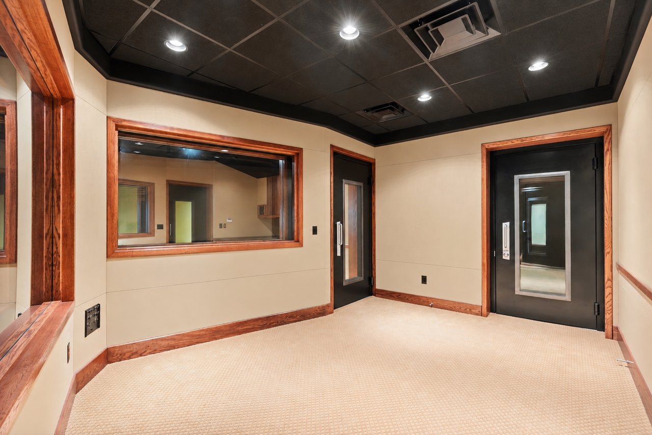 Sound-isolated studio room with a large interior window and black doors.