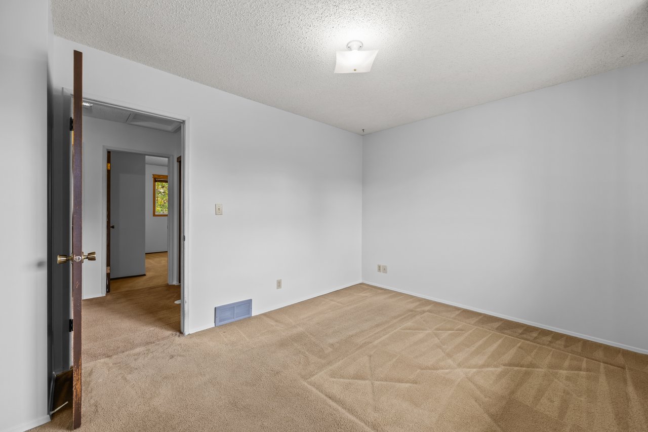 Empty bedroom with beige carpet and an open doorway to the hall.
