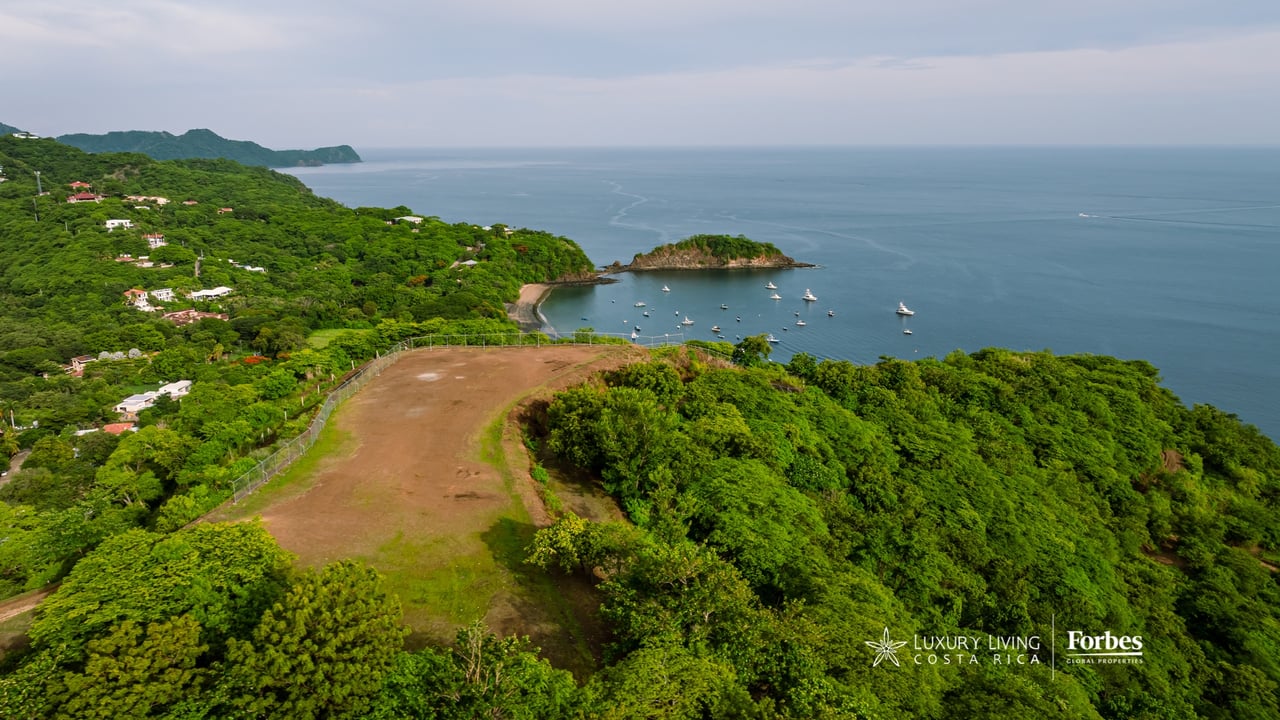 Cleared residential lot bordered by tropical forest, overlooking a boat-filled bay and the ocean.