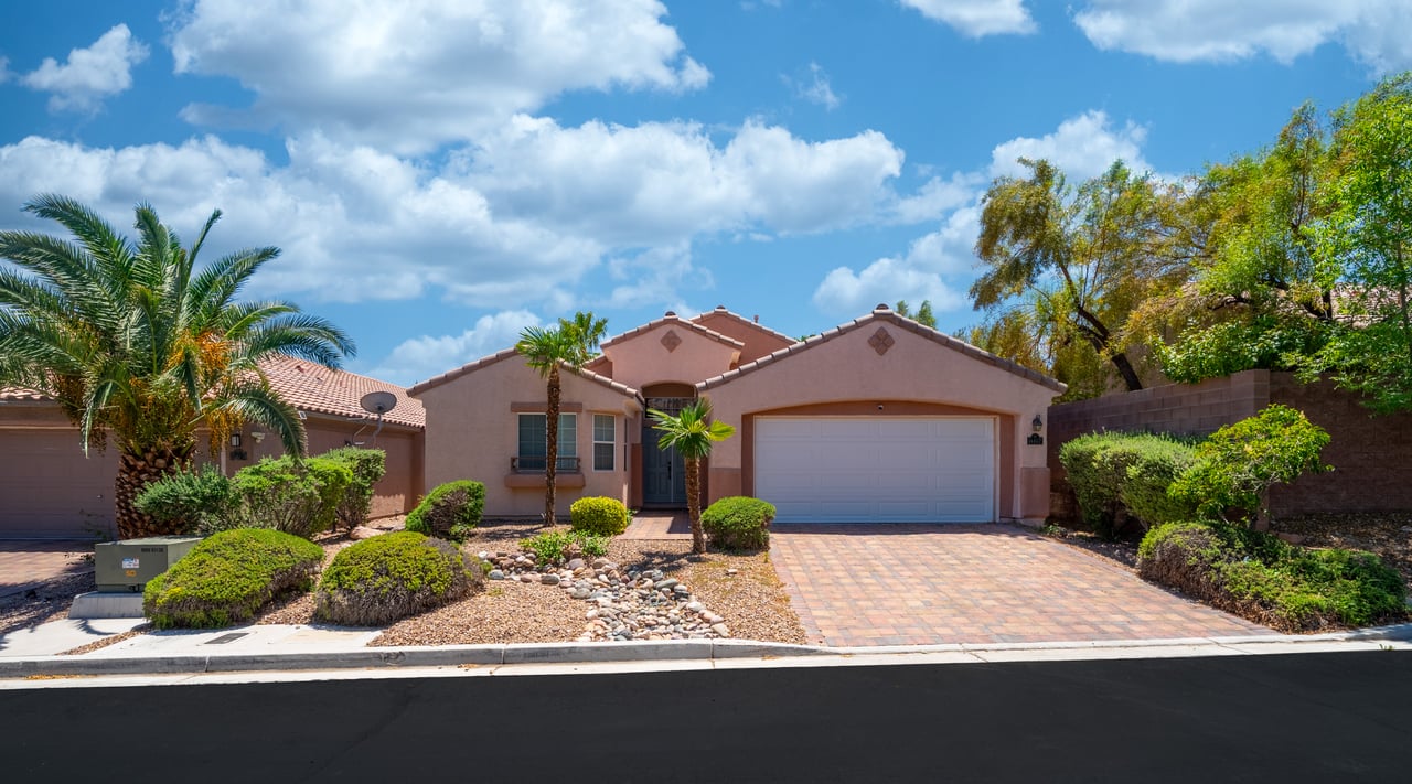 Pink stucco home with a tiled roof, two-car garage, paved driveway, and palm-lined desert landscaping.