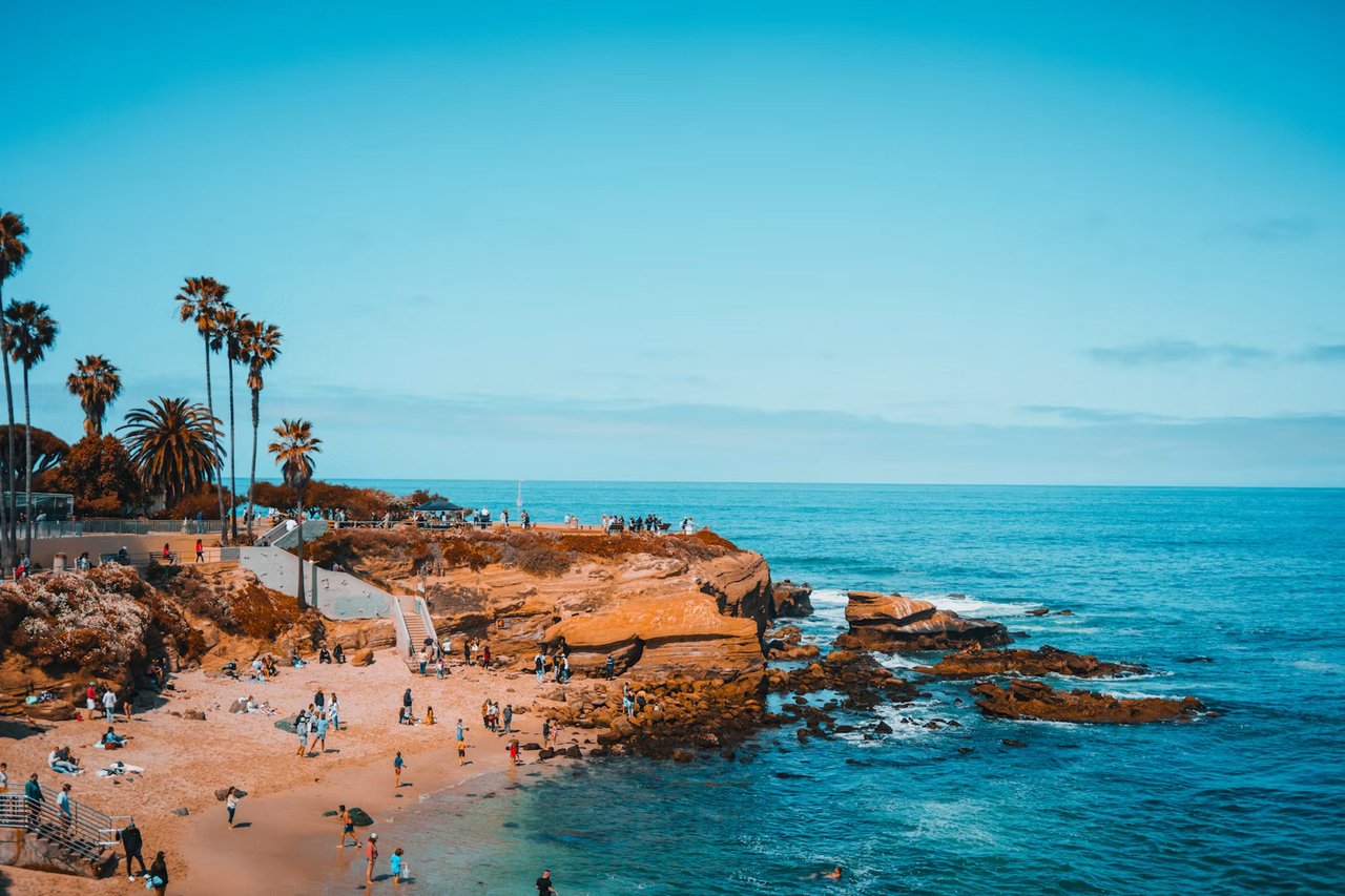 San Diego coastline with ocean views, palm trees, rocky shoreline, and beachgoers along the Southern California coast.