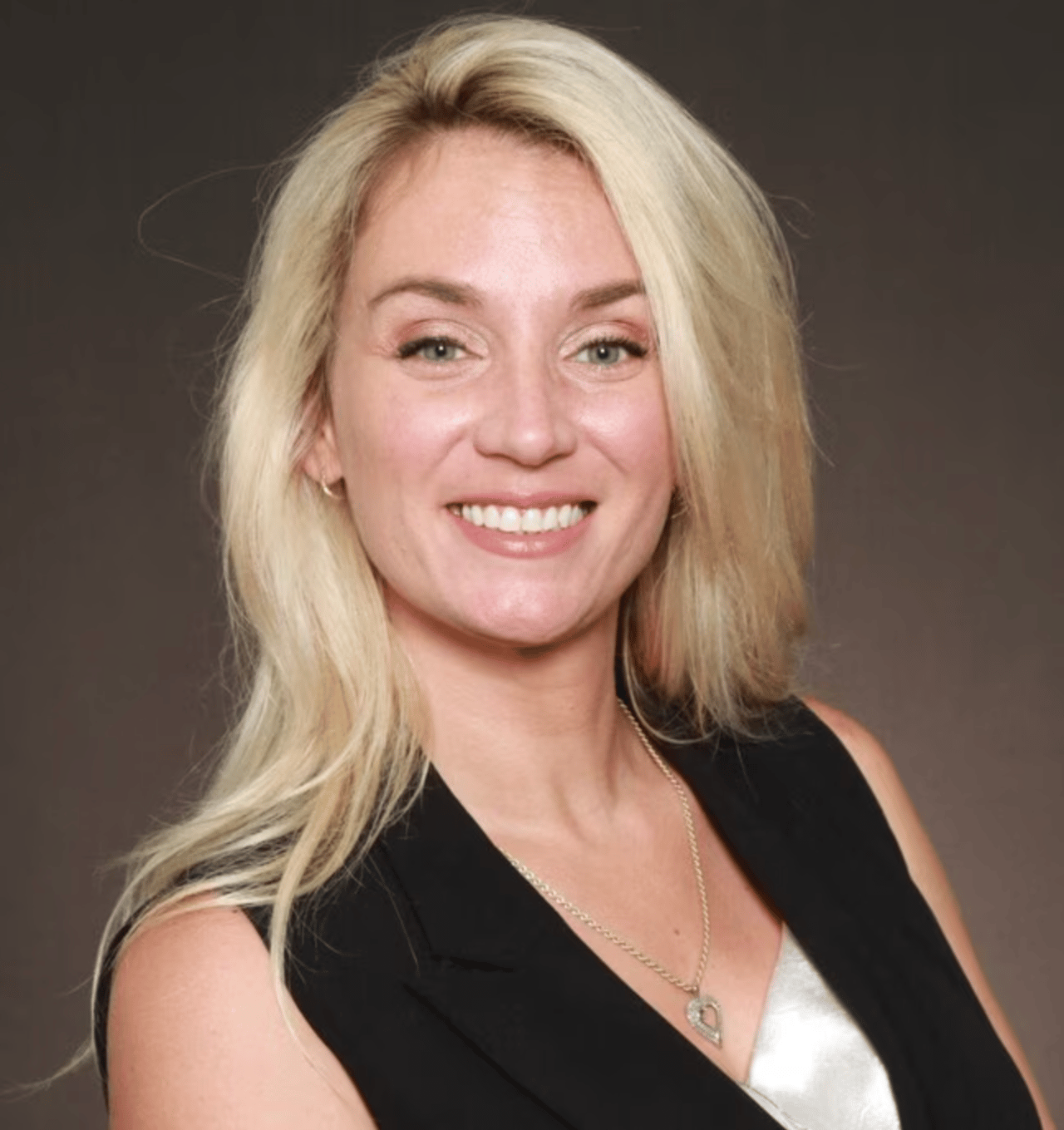 Laura Dochwat smiling in a black vest and pendant necklace.
