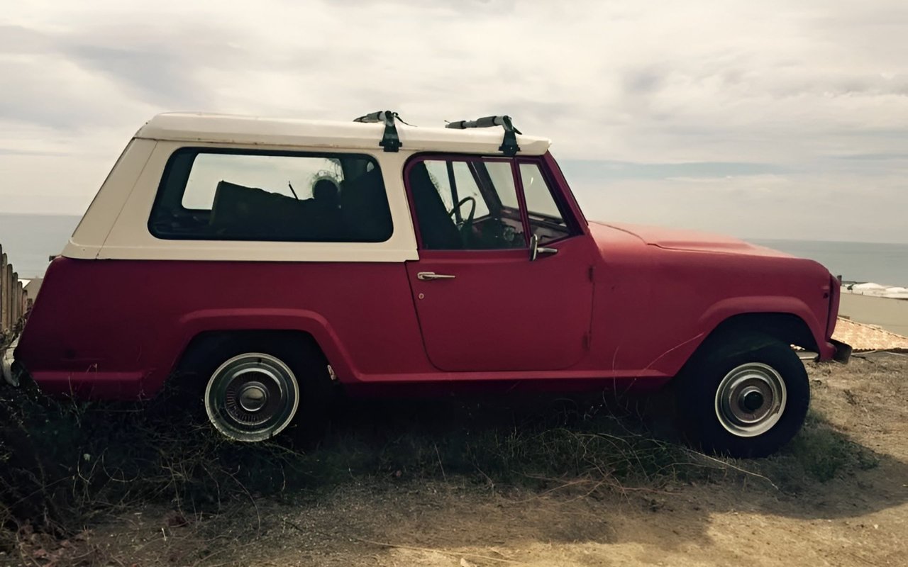 Red vintage off-road vehicle with a white roof parked above the ocean.