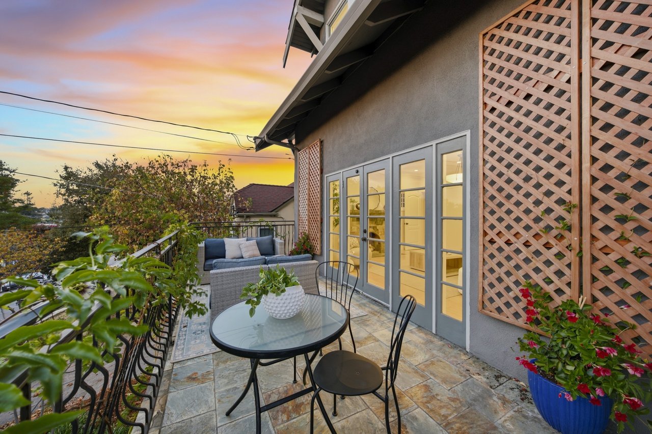 Outdoor patio with tiled flooring, a glass dining table, cushioned seating, and French doors at sunset.