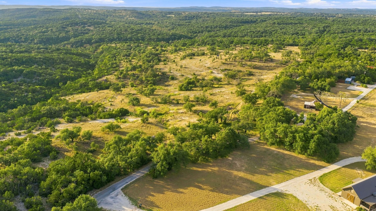 Aerial view of a Texas Hill Country ranch with wooded hills, an open clearing, and winding roads.