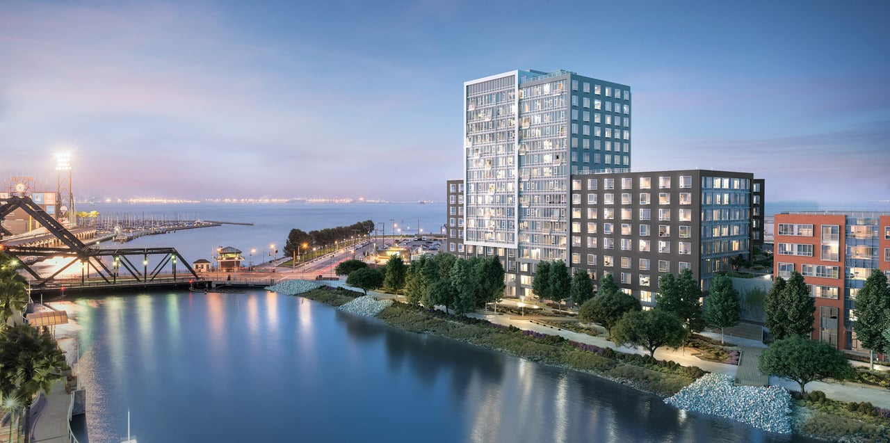 Waterfront condominium buildings at dusk, with illuminated windows beside a bridge and calm water.
