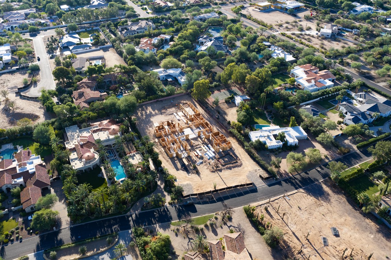 Aerial view of homes under construction amid landscaped neighboring residences and pools.