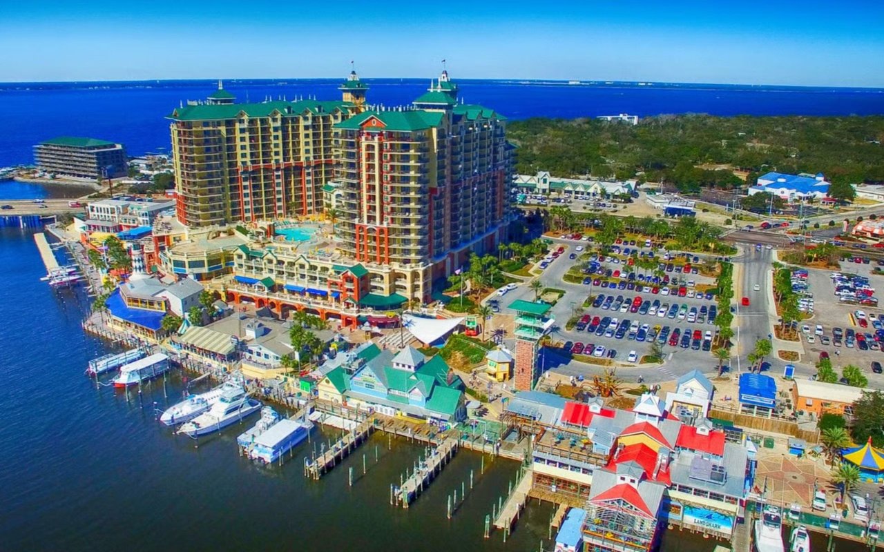 Waterfront resort and marina with a green-roofed high-rise, docks, and boats along the Gulf.