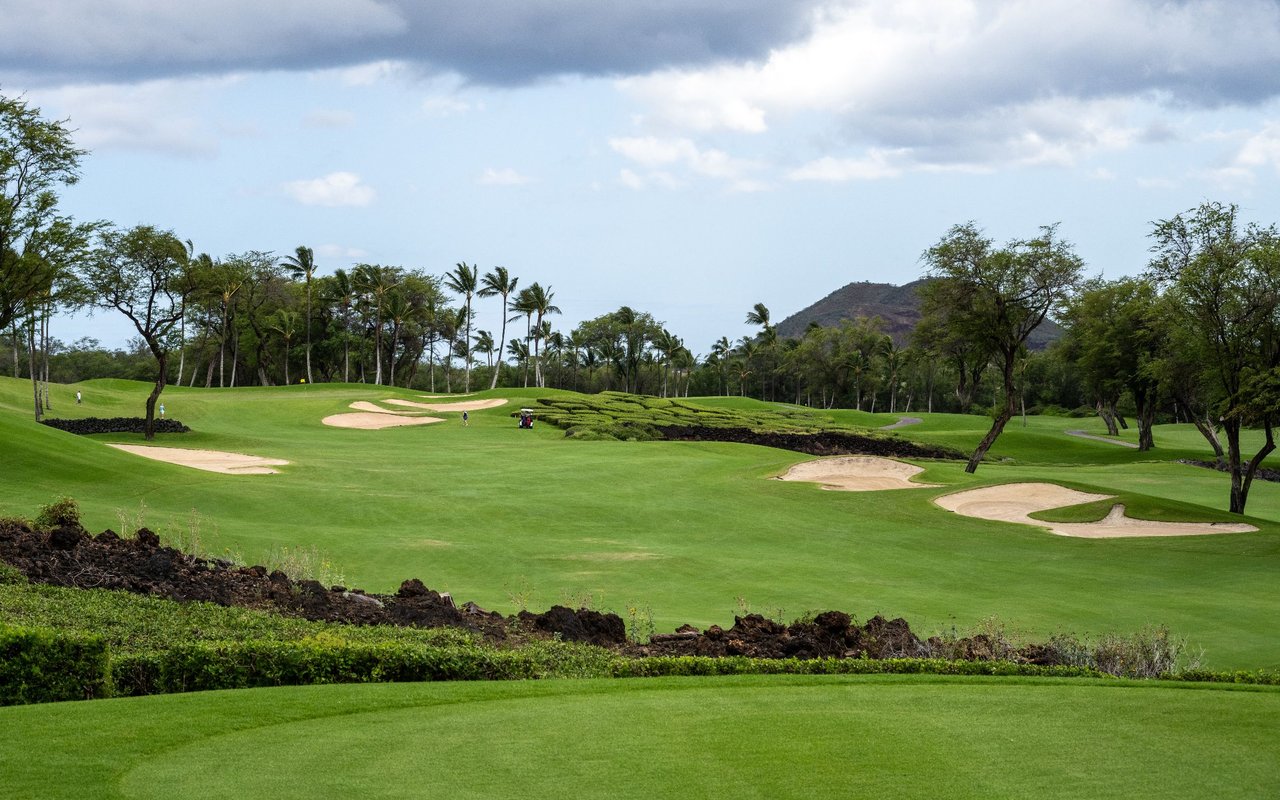 Golf course with sand bunkers and palm trees, backed by a low hillside.