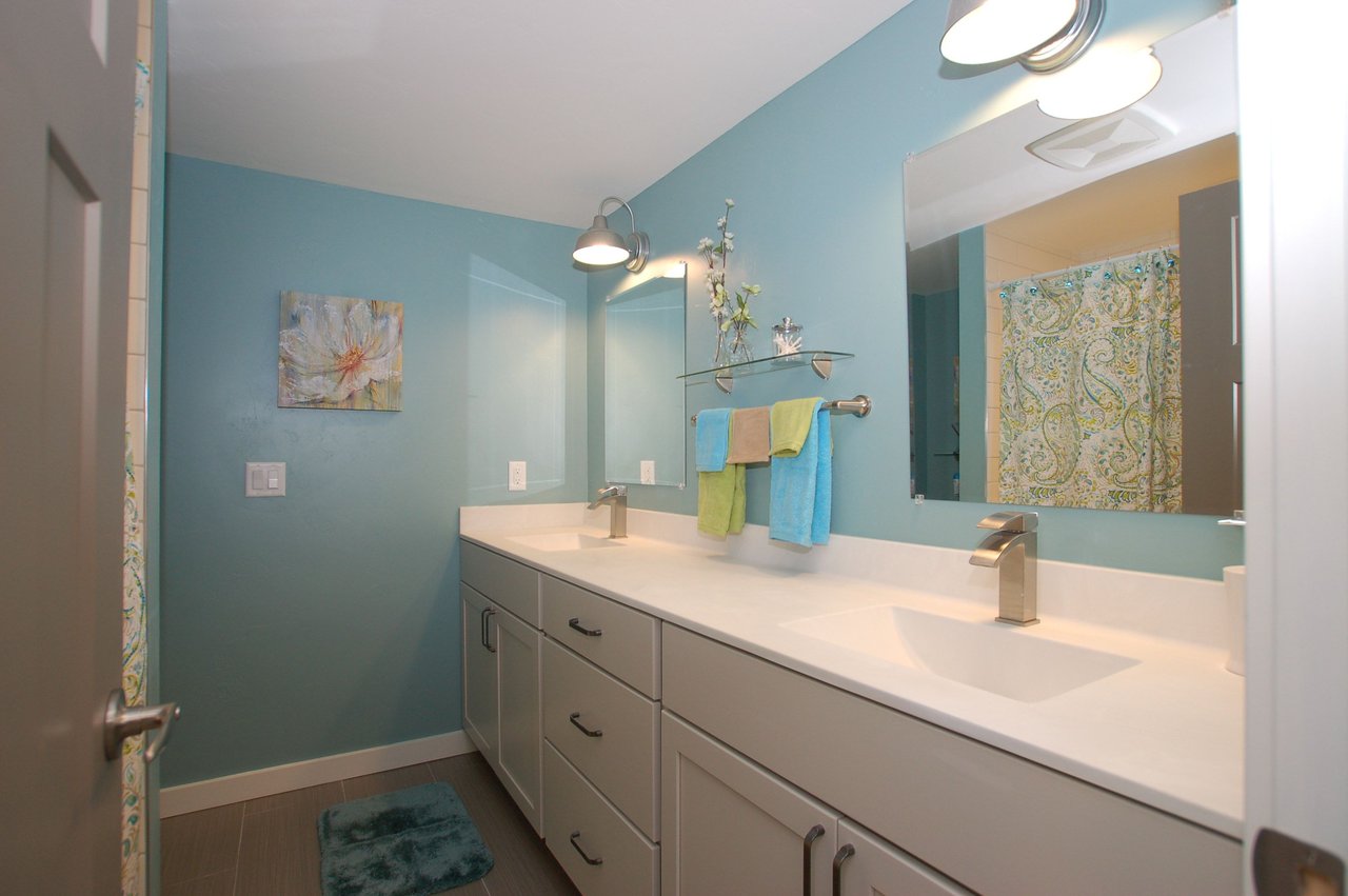 Bathroom with a long double-sink vanity, teal walls, and colorful towels.
