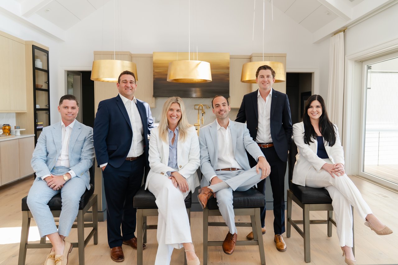 Six real estate agents posed together in a bright modern kitchen.