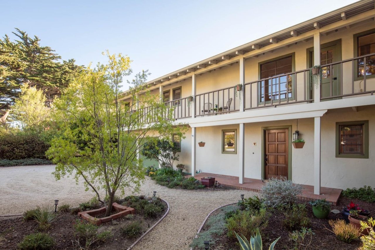 Two-story cream building with a long balcony, gravel walkway, and landscaped courtyard.